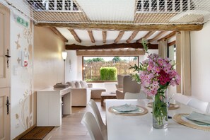 Ein modernes Interieur mit Essbereich, weißen Möbeln, einer klaren Vase mit Blumen und Blick durch ein Fenster.