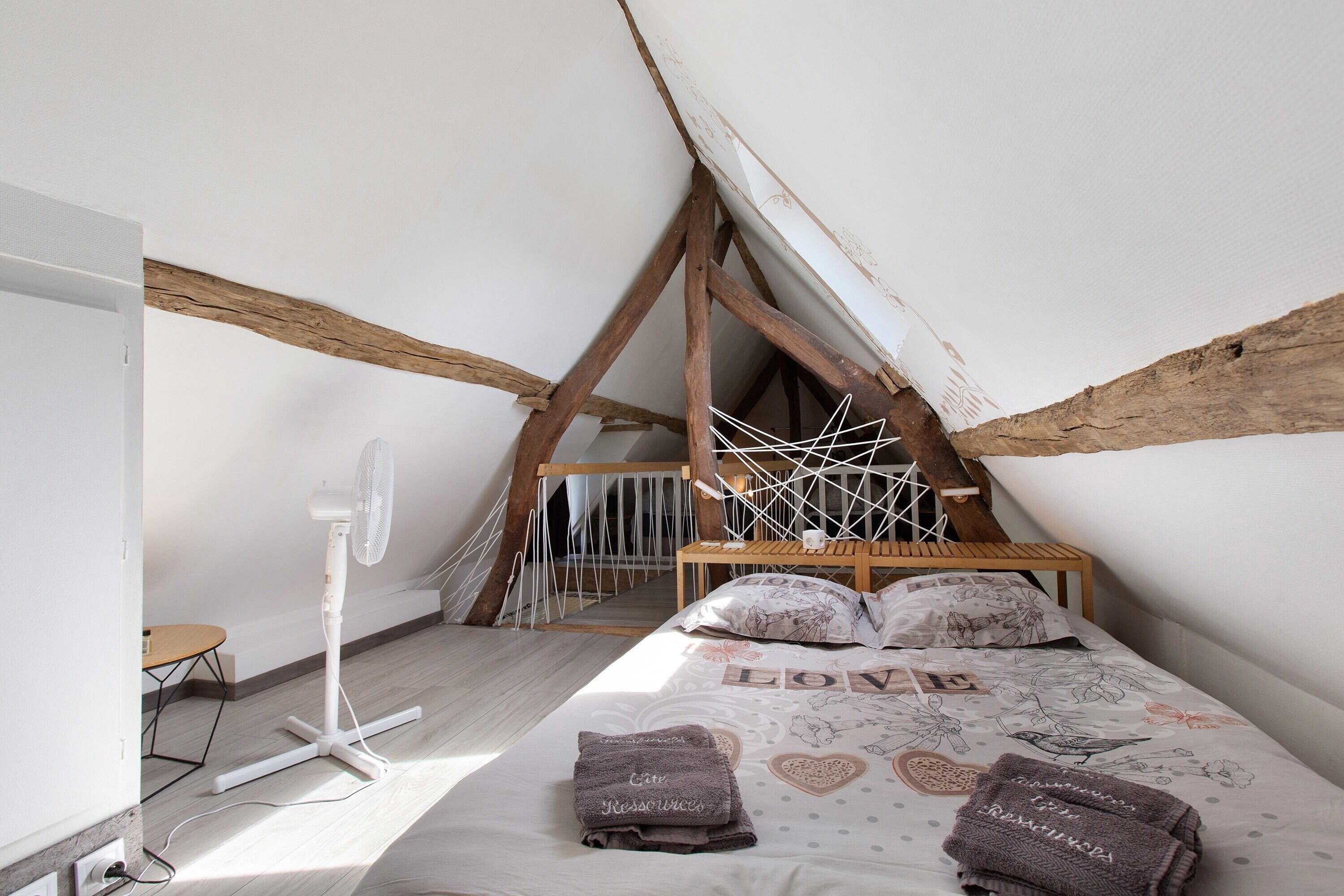 Un dormitorio con techo inclinado, una cama con cubrecama floral y un ventilador de pie.