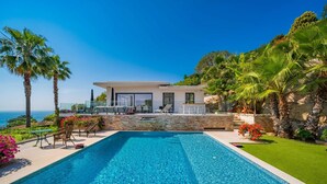 Un área moderna junto a la piscina con vista despejada al océano, una pared de piedra y un edificio con amplios ventanales.