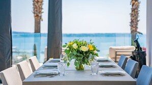 Mesa de comedor dispuesta con platos, cubiertos y un centro de mesa floral, con vista a un cuerpo de agua.