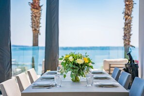 A dining table set with plates, cutlery, and a floral centerpiece, overlooking a body of water. - Contemporary sea view villa with pool, near Cannes (Vallauris)