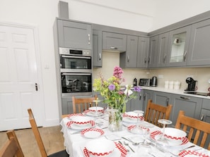 Une cuisine avec des meubles gris, une porte blanche et une table à manger dressée avec des assiettes et un vase de fleurs.