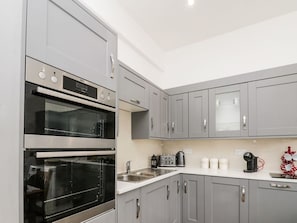 Une cuisine moderne avec des meubles gris, un four double, une machine à café et un grille-pain.