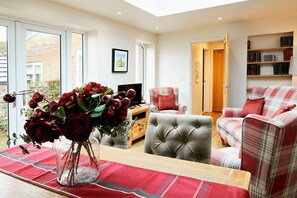 Ein Wohnzimmer mit einer Couch, einem Sessel und einer Glasvase mit Blumen.