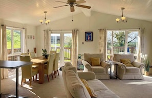 A spacious room with a dining area, two sofas, a ceiling fan, and large windows. - Lowena Lodge, Millbrook (Torpoint)