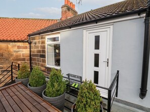 A building with a white door, a window, and a brick wall. There are potted plants and a bench outside. - Postman’s Lodge, Great Ayton (Middlesbrough)