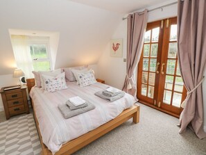 A bedroom with a wooden bed, a nightstand, a lamp, a window with curtains, and a view of the outdoors. - North Studdock Cottage, Pembroke (Pembroke)
