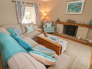 A living room with a beige sofa, a patterned coffee table, a blue armchair, a fireplace, and a painting on the wall. - North Studdock Cottage, Pembroke (Pembroke)