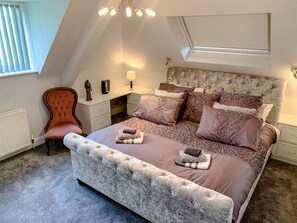 A bedroom with a large bed, a chair, a nightstand, a lamp, and a window. - The Gables Penthouse in Dorset (Poole)