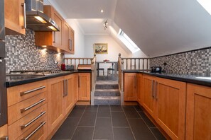 A modern kitchen with wooden cabinets, a tiled backsplash, a built-in stove, and a staircase leading to a dining area. - The Gables Penthouse in Dorset (Poole)