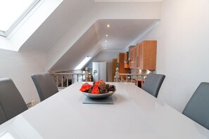 A modern kitchen with a skylight, a dining table with chairs, and a bowl of pinecones and red flowers. - The Gables Penthouse in Dorset (Poole)