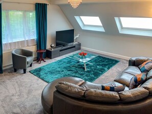 A modern living room with a sofa, a glass coffee table, a television, and a skylight. - The Gables Penthouse in Dorset (Poole)