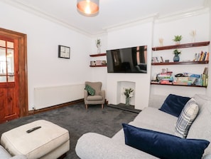 A living room with a sofa, ottoman, fireplace, TV, bookshelf, and a clock on the wall. - Castle Manor is in Scarborough (Scarborough)