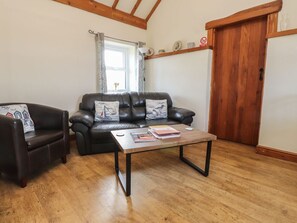 A living room with a leather sofa, a wooden coffee table, and a wooden floor. - Hen Stabl at Tyn Llan, Cemaes Bay (Cemaes Bay)