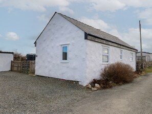 A single-story white building with a sloped roof, a small window, and a gravel driveway. - Hen Stabl at Tyn Llan, Cemaes Bay (Cemaes Bay)