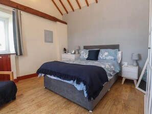A bedroom with a large bed, bedside tables, a window with curtains, and a wooden floor. - Hen Stabl at Tyn Llan, Cemaes Bay (Cemaes Bay)