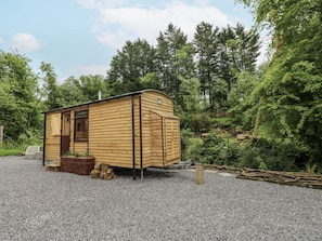 A small wooden cabin with a door and windows, surrounded by gravel and trees. - The Hamper, Carmarthen (Carmarthen)