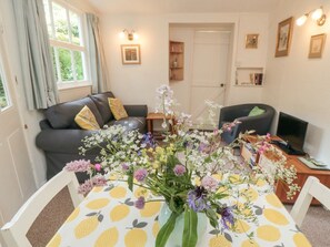 A living room with a sofa, a dining table with a vase of flowers, and a television. - Damson Croft, Lastingham (York)