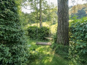 A wooden swing in a lush garden with dense foliage and a large tree trunk. - Damson Croft, Lastingham (York)