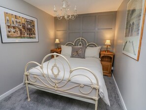 A bedroom with a bed, two bedside tables, a chandelier, and framed artwork on the walls. - Inglis Nook Cottage Retreat (Lochearnhead)