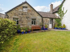 A stone house with a grassy yard, a wooden bench, and potted plants. - Inglis Nook Cottage Retreat (Lochearnhead)
