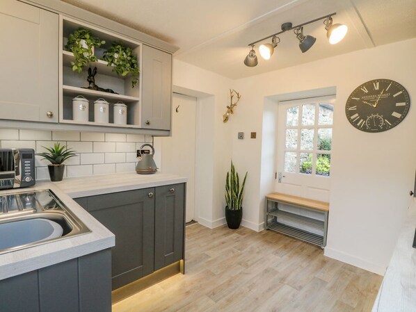 A kitchen with a sink, cabinets, a clock, and a window. - Inglis Nook Cottage Retreat (Lochearnhead)