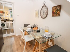 A dining area with a glass table, white chairs, a clock, and a painting on the wall. - Rosewood Cottage, Flamborough (Bridlington)