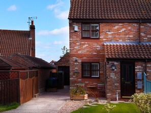 A brick house with a tiled roof, a front door, and a small garden area with a bench and potted plants. - Rosewood Cottage, Flamborough (Bridlington)