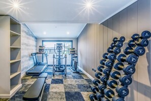 Ein Fitnessraum mit Laufbändern, Crosstrainern und einer Wand voller Kurzhanteln.