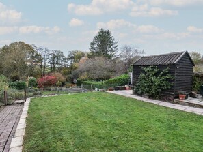 A well-maintained garden with a wooden shed, a paved pathway, and various shrubs and trees.