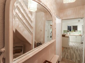 A hallway leading to a staircase and a kitchen area with cabinets and a countertop.