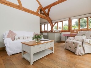 Ein gemütliches Zimmer mit Holzbalkendecke, einem weißen Sofa, einem Holztisch und einem gemusterten Sofa.