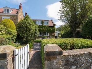 Eine Steinsäule, ein weißes Tor und ein Weg zu einem Haus mit roten Ziegeln.