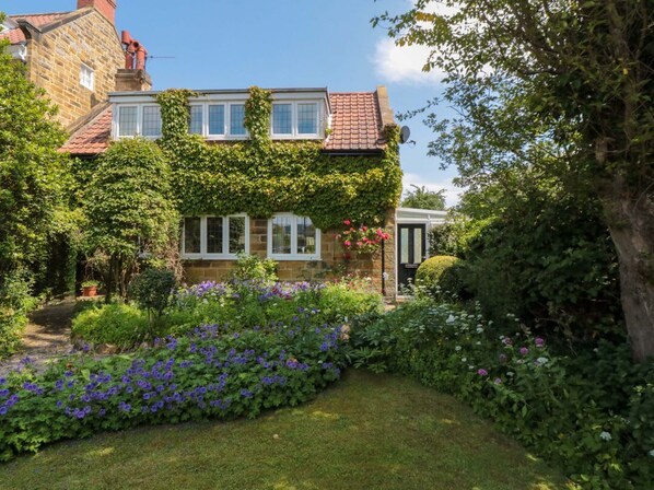 A stone house with ivy-covered walls, a garden with purple flowers, and a clear blue sky. - Scalby Grove Cottage, Scalby (Scarborough)