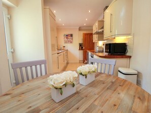 Eine Küche mit Holzausstattung, einer Mikrowelle und einem Esstisch mit weißen Tischdekorationen mit Blumenmuster.