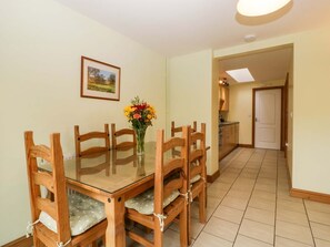 Ein Essbereich mit einem Tisch mit Glasplatte, Holzstühlen mit gepolsterten Sitzen, einer Vase mit Blumen und einem gerahmten Bild an der Wand.