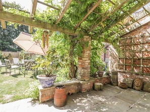 Ein überdachter Patio-Bereich mit Backsteinmauer, Kübelpflanzen und Gartenmöbeln.