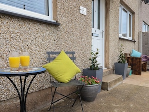A patio with a metal table, two glasses of orange juice, a green cushion, and potted plants. - Gwynfa in Rhyd Uchaf, Gwynedd. (Bala)