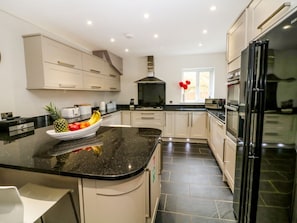 A modern kitchen with a black granite countertop, white cabinets, a stainless steel range hood, and a black refrigerator.