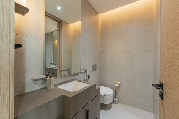 A modern bathroom with a sink, mirror, toilet, and shower area. - Live the Vibe: Upgraded 2BR | JBR Coastal Living (Dubai)