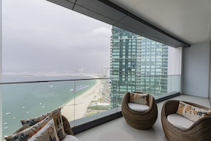 Ein Balkon mit Korbstühlen, einer Glasreling und Blick auf Strand und Hochhäuser.