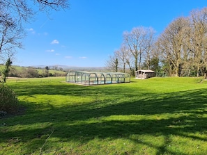 A greenhouse structure in a grassy field with a small building nearby.
