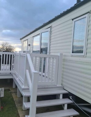 A mobile home with a white exterior, a porch with white railings, and a window with a view of the sky.