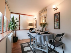 Un comedor con una mesa dispuesta para dos personas, una planta en maceta y una ventana con persianas.