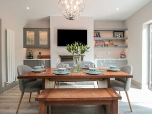 A dining area with a wooden table set for four, a vase with green plants, and a modern kitchen in the background. - 41 Chatsworth Gardens, 4 beds. (Scarborough)