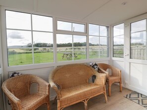A sunroom with wicker furniture and large windows overlooking a grassy area. - Arthur's Cottage, in Kirkbean. (Dumfries)
