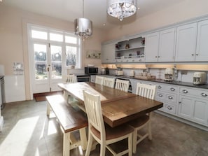 Une cuisine avec une table et des chaises en bois, des armoires blanches et un lustre.