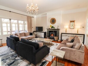 Un salon moderne avec une cheminée, des canapés, un téléviseur et un lustre.