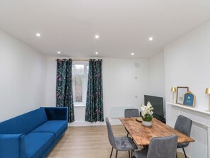 Una habitación moderna con un sofá azul, una mesa de comedor de madera con sillas, un televisor y una chimenea.