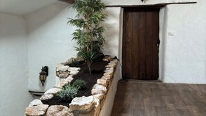 Una stanza con travi a vista in legno, un vaso in pietra con una pianta di bambù, una porta in legno e un muro in pietra.